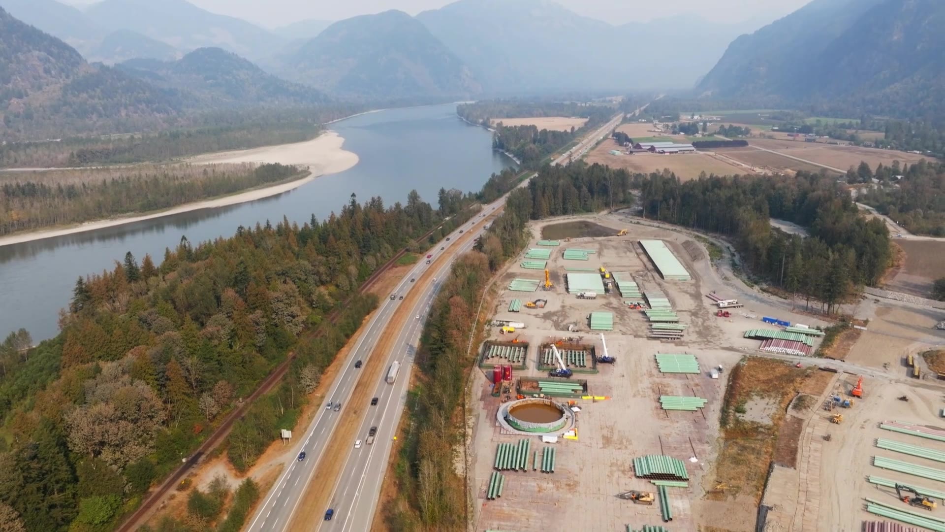 Aerial view of a Canadian pipeline construction yard staging pipe along a river valley