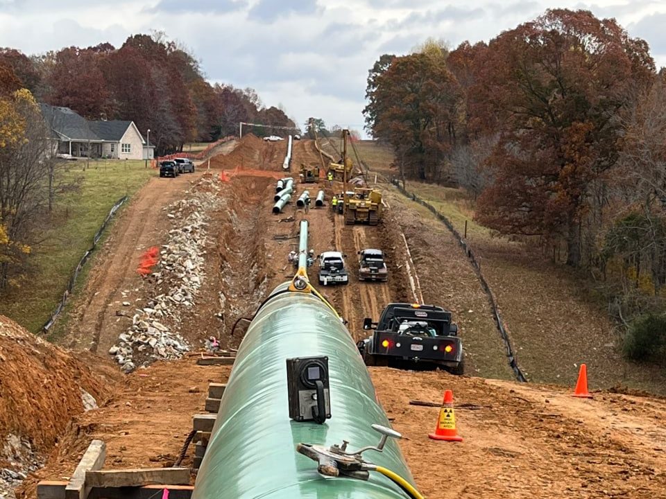 Welded transmission pipe strung down a wooded right-of-way with the inspection spread working the ditch