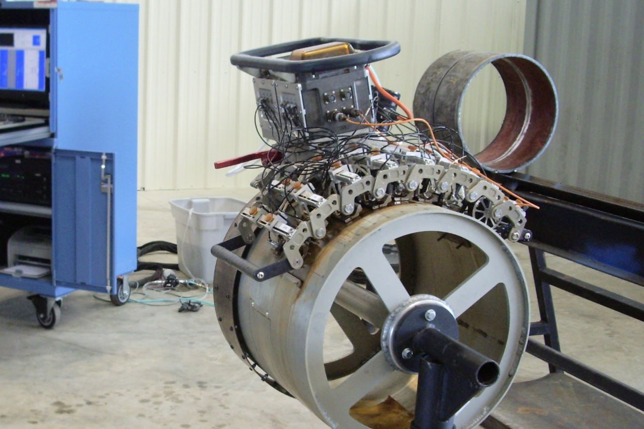 Blue AUT data-acquisition cabinet beside an automated ultrasonic scanner band and crawler clamped on a pipe joint
