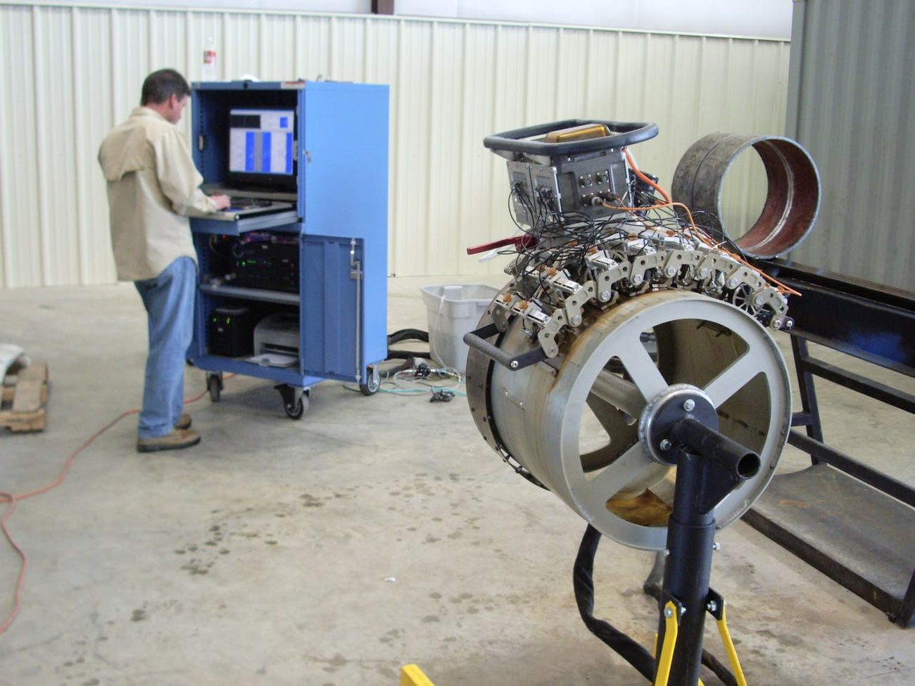 Technician at the AUT acquisition station beside a large-diameter automated ultrasonic scanner in the shop