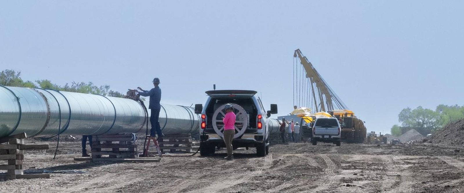 Pipe strung on skids with a crane and inspection trucks working a U.S. right-of-way